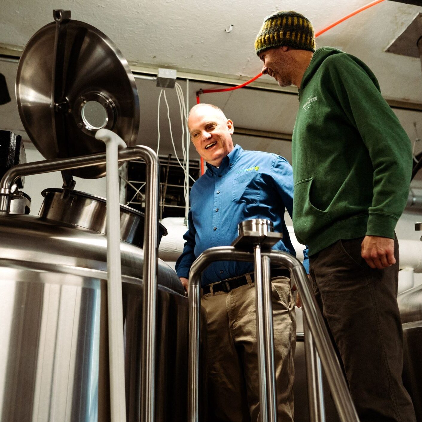 Maine MEP project manager stands in a brewery with business owner looking at each other and laughing.